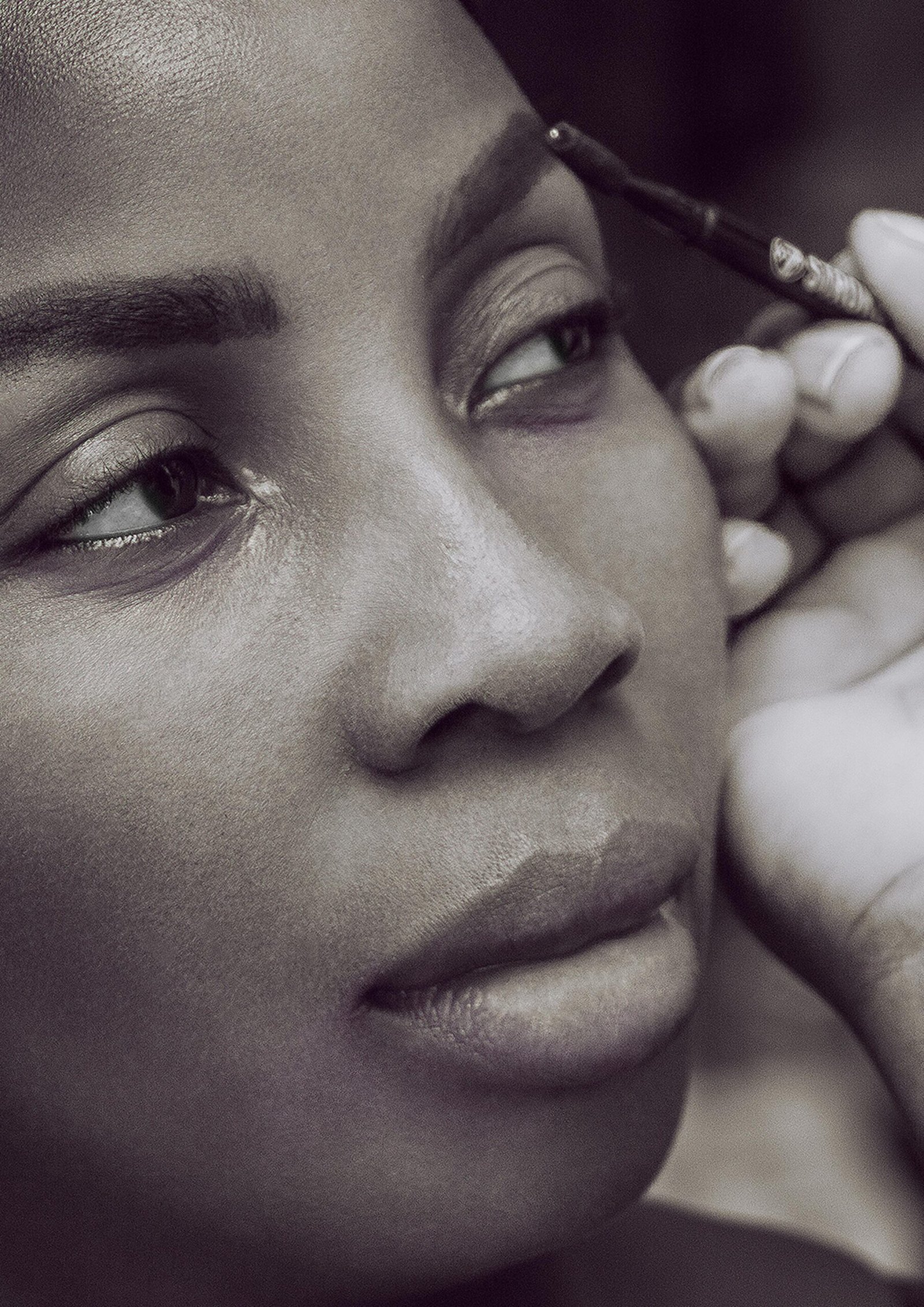Black and white portrait of a woman having her eyebrows applied with makeup.
